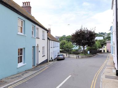 A street with pastel colored houses and a parked car near a tree at Bedrock in Lyme Regis