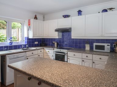 A kitchen with white cabinets blue tile backsplash and speckled countertops at 2 Kersbrook Gardens Lyme Regis