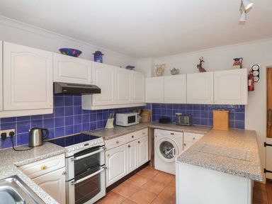 A kitchen with white cabinets blue tile backsplash and various appliances including stove microwave and washing machine at 2 Kersbrook Gardens in Lyme Regis