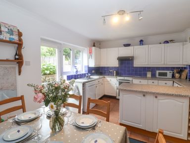 A kitchen with a dining table set with plates and glasses and white cabinets with blue tiled backsplash at 2 Kersbrook Gardens in Lyme Regis