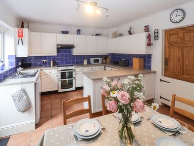 A kitchen with white cabinets blue tiled backsplash wooden dining chairs and a table with a floral centerpiece at 2 Kersbrook Gardens Lyme Regis