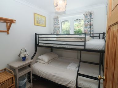 A small bedroom with a black metal bunk bed next to a window with printed curtains and a small table with a lamp beside it at 2 Kersbrook Gardens in Lyme Regis