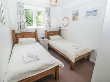 A bedroom with two single beds a nightstand and window curtains at 2 Kersbrook Gardens Lyme Regis
