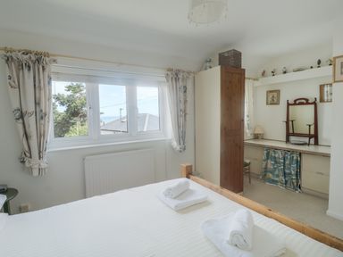 A bedroom with a bed, rolled towels, window with curtains, wardrobe, and a dressing table at 2 Kersbrook Gardens in Lyme Regis