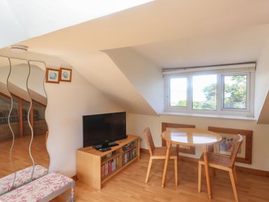 A room with a round wooden table and two chairs a TV on a wooden stand and a window showing trees at 2 Kersbrook Gardens in Lyme Regis