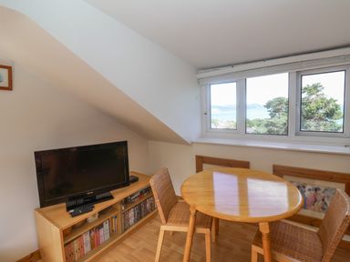 A dining area with a round wooden table and two wicker chairs next to a window showing a sea view at 2 Kersbrook Gardens in Lyme Regis