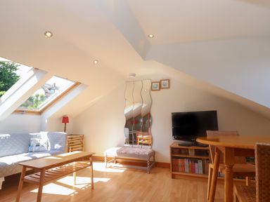 A living room with a sofa coffee table bench television and dining table at 2 Kersbrook Gardens Lyme Regis