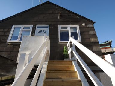 Wooden stairs with white railings leading to a door and windows on the upper floor of a dark shingled building at 11 The Gables in Lyme Regis