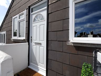 A white front door with the number 11 on a brown tiled exterior wall with windows at 11 The Gables Lyme Regis