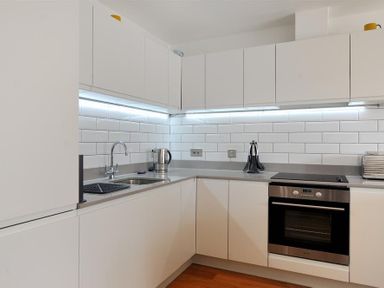 A kitchen with white cabinets a built in oven a kettle and utensils on the counter at The Lower Deck in Lyme Regis
