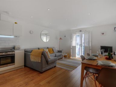 A living room with a grey sofa and yellow cushions next to a dining table set with dishes and glasses at The Lower Deck in Lyme Regis