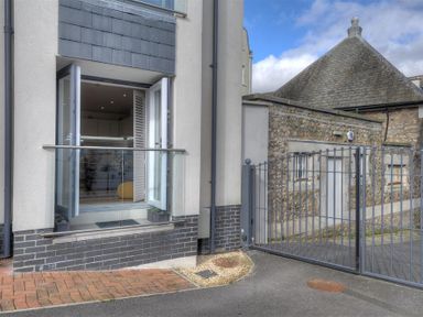 An open doorway with glass railing next to a metal gate and stone building exterior