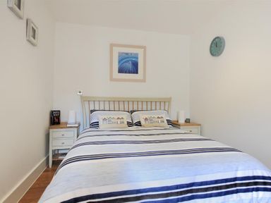 A bedroom with a double bed with striped bedding two bedside tables a wall clock and a framed picture above the bed at The Lower Deck in Lyme Regis