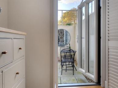A small outdoor patio with a round metal table and three metal chairs a bottle and glass on the table and a circular wall mirror at The Lower Deck in Lyme Regis
