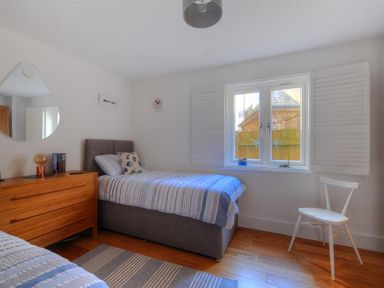 A bedroom with two single beds a wooden dresser a triangular mirror a white chair and a window with shutters at The Lower Deck in Lyme Regis