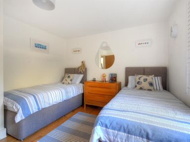 A bedroom with two single beds a wooden chest of drawers and a wall mirror at The Lower Deck in Lyme Regis