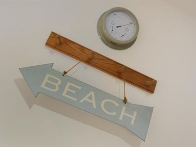 A wooden coat rack with a hanging blue arrow sign that says beach and a wall-mounted weather station above it