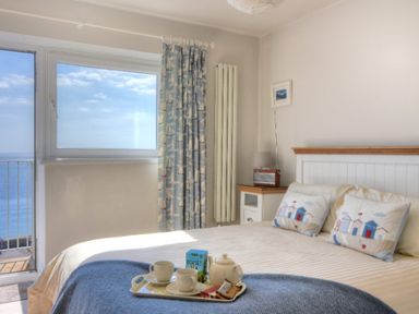 A bedroom with a bed and breakfast tray next to a window with sea view at 9 Bay View Court Lyme Regis