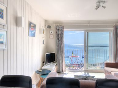 A living room with a television small tables and chairs with a sea view at 9 Bay View Court in Lyme Regis