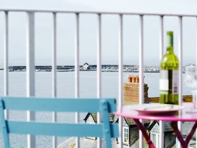 A balcony with a blue chair pink table a bottle of wine and a wine glass overlooking the sea and a harbor at 9 Bay View Court in Lyme Regis