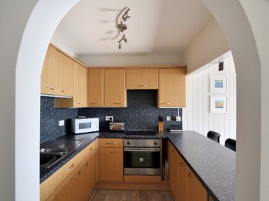 A kitchen with wooden cabinets black countertops a microwave a toaster a stove and two framed pictures on the wall at 9 Bay View Court in Lyme Regis