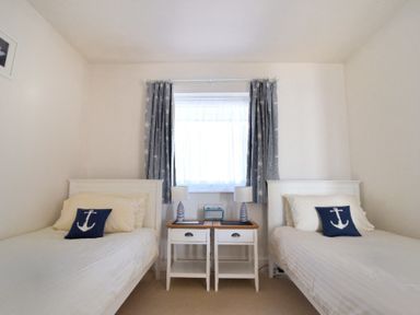 A bedroom with two single beds and a window with curtains at 9 Bay View Court in Lyme Regis
