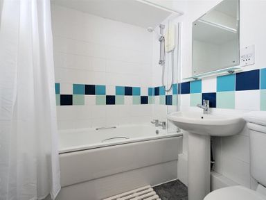 A bathroom with a bathtub shower white curtain pedestal sink and toilet at 9 Bay View Court Lyme Regis
