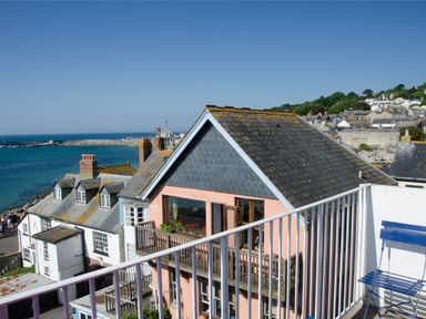View of coastal houses with a balcony railing and a blue chair overlooking the sea at 9 Bay View Court in Lyme Regis
