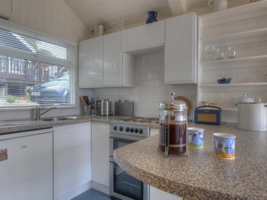 A kitchen with white cabinets coffee press mugs and stove at 8 Bowling Green Chalets in Lyme Regis