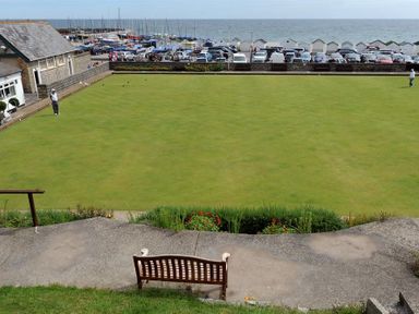 A lawn bowling green with players near a building parking and boats in the background at 8 Bowling Green Chalets in Lyme Regis