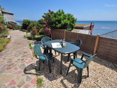 An outdoor patio area with a plastic table and four chairs on gravel next to a stone pathway overlooking the sea at Ross House Lyme Regis
