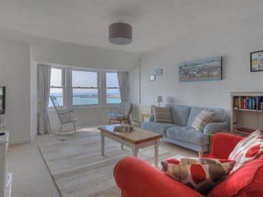 A living room with red and blue sofas a coffee table a rocking chair and a window showing a sea view at Ross House in Lyme Regis