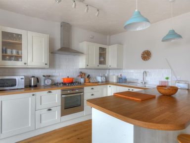 A kitchen with white cabinets wooden countertops a stove microwave kettle and hanging lights at Ross House in Lyme Regis