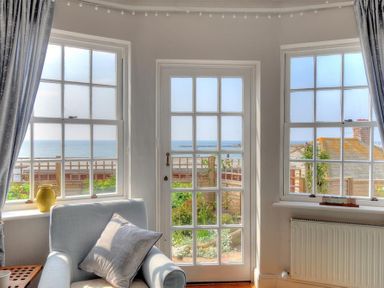 A room with a light blue armchair and a pillow near windows and a glass door with a view of the ocean at Ross House Lyme Regis