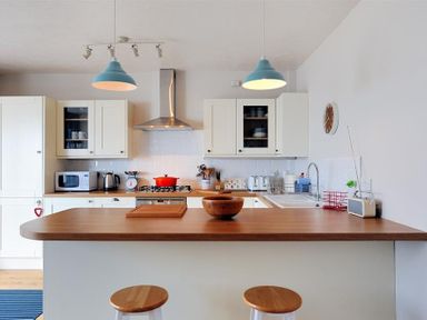 A kitchen with a wooden countertop island two stools hanging blue lamps and white cabinets at Ross House in Lyme Regis