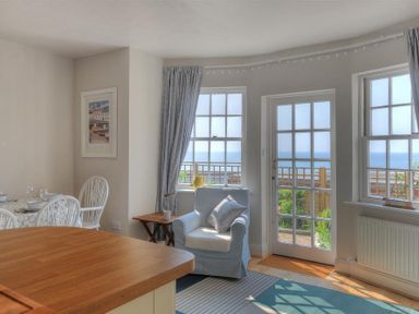 A sitting area with an armchair a wooden table and dining chairs near windows and a glass door overlooking the sea at Ross House in Lyme Regis