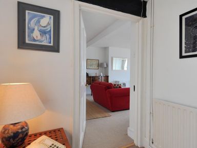 A view through a doorway showing a red sofa in a living room with a lamp and pictures on walls at Ross House in Lyme Regis