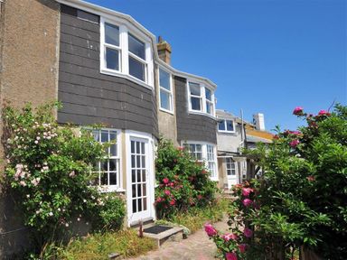 Exterior view of a house with multiple white windows a glass door and flowering plants in front at Ross House in Lyme Regis