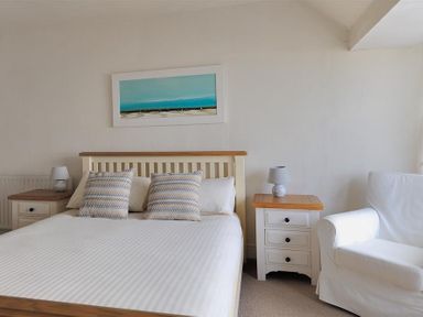 A bedroom with a bed two striped pillows two bedside tables with lamps a white armchair and a painting on the wall at Ross House in Lyme Regis