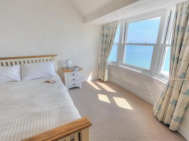 A bedroom with a bed bedside table lamp and a large window overlooking the sea at Ross House in Lyme Regis
