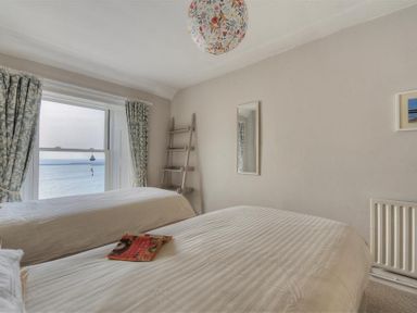 A bedroom with two beds a window showing a sea view curtains a small ladder and a mirror on the wall at Ross House in Lyme Regis