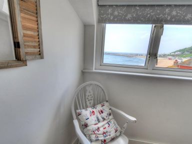 A white chair with a patterned cushion under a window showing a seaside view at Ross House in Lyme Regis