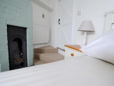 A bedroom corner with a bed pillow a bedside table lamp a green painted brick fireplace stairs and a white door at Ross House in Lyme Regis