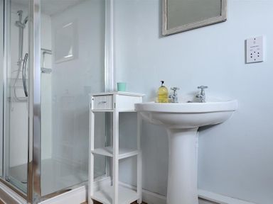A bathroom with a shower enclosure a white pedestal sink a small white storage unit and a mirror at Ross House in Lyme Regis