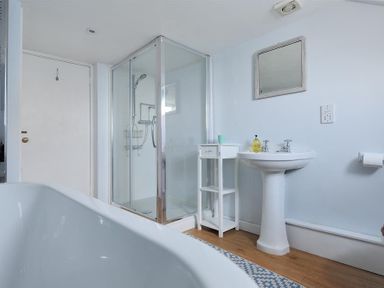 A bathroom with a bathtub shower enclosure pedestal sink small shelf and mirror at Ross House in Lyme Regis