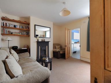 A living room with a beige sofa and armchair a black fireplace and shelves with books at 23 Lym Close in Lyme Regis