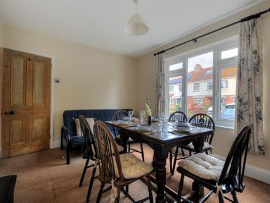 A dining room with a wooden table set for six and a sofa near a window at 23 Lym Close in Lyme Regis