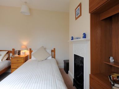 A bedroom with two single beds a wooden nightstand a lamp a fireplace and shelving at 23 Lym Close Lyme Regis