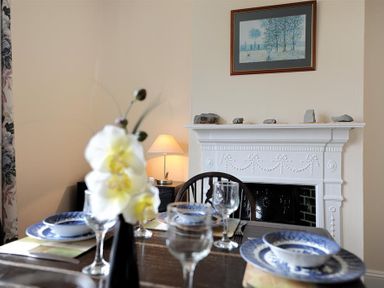 A dining area with a table set with blue and white plates and bowls a white decorative fireplace with stones on the mantel and a framed picture above at 23 Lym Close Lyme Regis