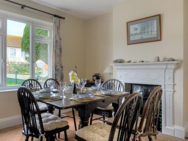 A dining room with six chairs around a table set with dishes and glasses near a fireplace with a framed picture above at 23 Lym Close Lyme Regis